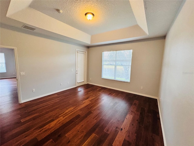 empty room with a raised ceiling, dark wood-type flooring, and a textured ceiling