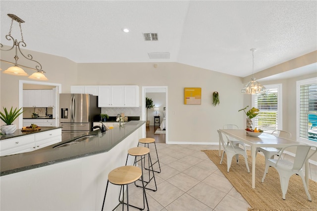 kitchen featuring vaulted ceiling, light tile patterned floors, decorative light fixtures, white cabinets, and stainless steel fridge with ice dispenser