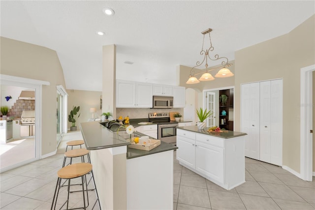 kitchen with kitchen peninsula, appliances with stainless steel finishes, white cabinetry, lofted ceiling, and light tile patterned flooring