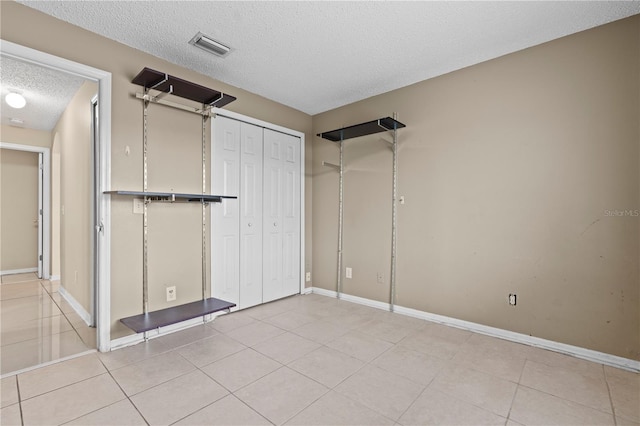 unfurnished bedroom with a closet, visible vents, light tile patterned flooring, a textured ceiling, and baseboards