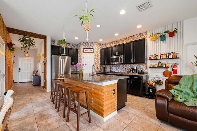 kitchen with sink, a breakfast bar area, appliances with stainless steel finishes, an island with sink, and dark stone counters