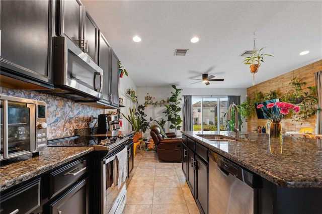 kitchen featuring sink, dark stone counters, light tile patterned floors, stainless steel appliances, and decorative backsplash