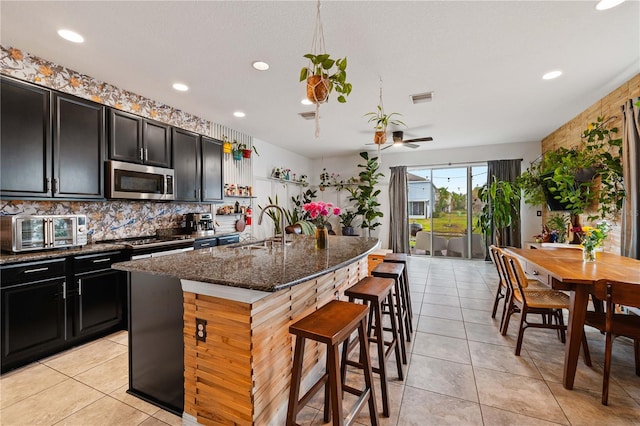 kitchen with sink, a breakfast bar area, a kitchen island with sink, stainless steel appliances, and dark stone counters