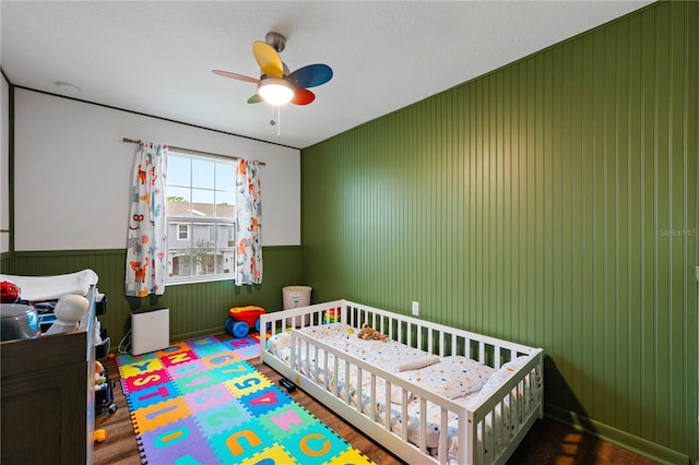 bedroom featuring ceiling fan, wooden walls, and a crib