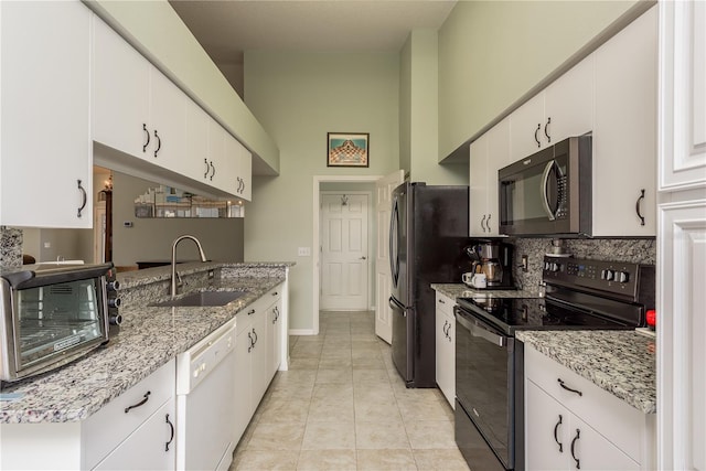 kitchen with black appliances, sink, light tile patterned flooring, light stone counters, and white cabinetry