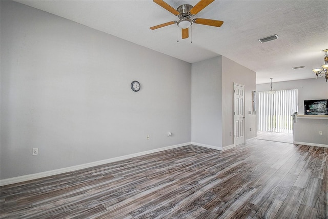 empty room with a textured ceiling, ceiling fan with notable chandelier, and dark wood-type flooring