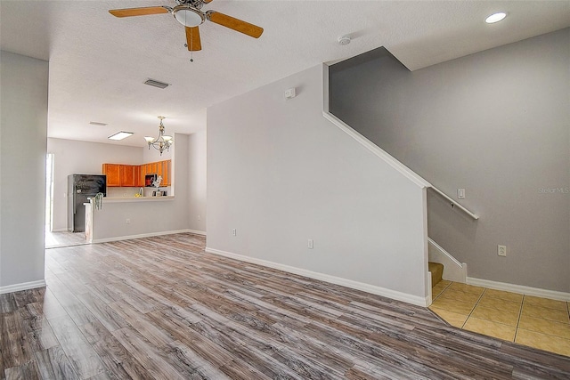 unfurnished living room with ceiling fan with notable chandelier, wood-type flooring, and a textured ceiling