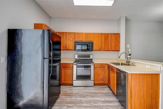 kitchen with kitchen peninsula, sink, black appliances, and light hardwood / wood-style floors