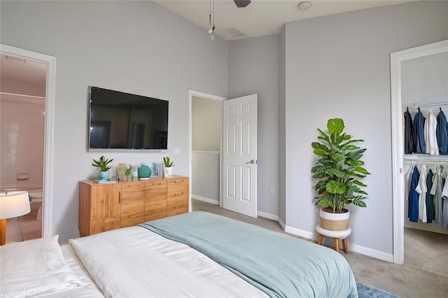 bedroom with ensuite bath, ceiling fan, a spacious closet, light colored carpet, and a closet