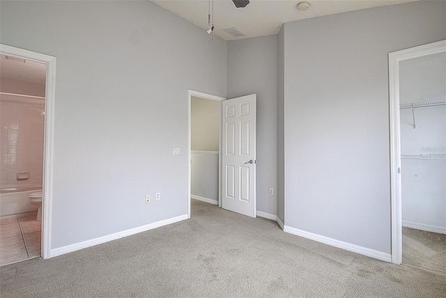 unfurnished bedroom featuring ceiling fan, a spacious closet, light carpet, and a closet