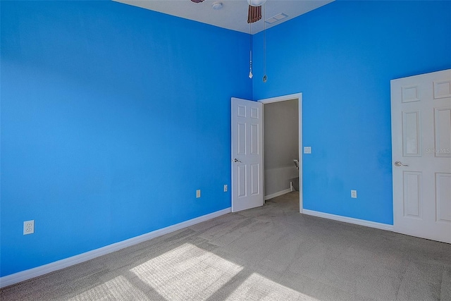 unfurnished bedroom featuring ceiling fan, carpet, and a high ceiling