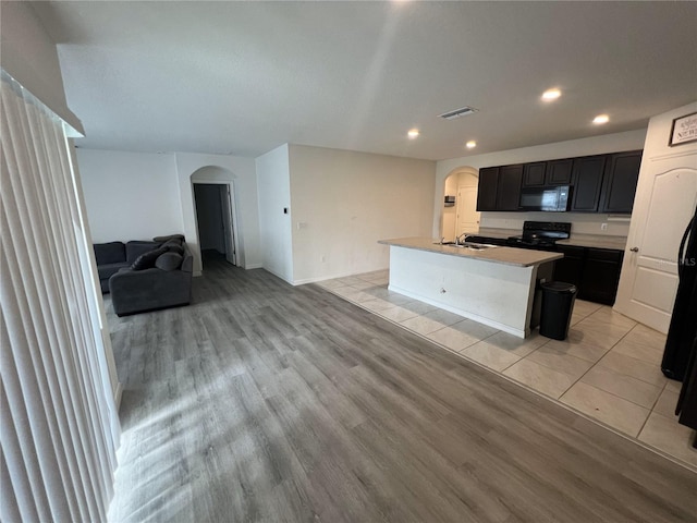 kitchen featuring black appliances, sink, light wood-type flooring, and an island with sink