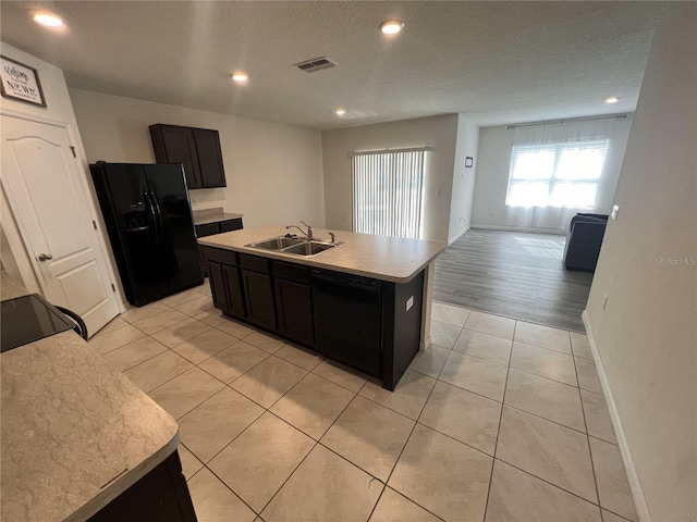 kitchen with a textured ceiling, sink, black appliances, a center island with sink, and light tile patterned flooring