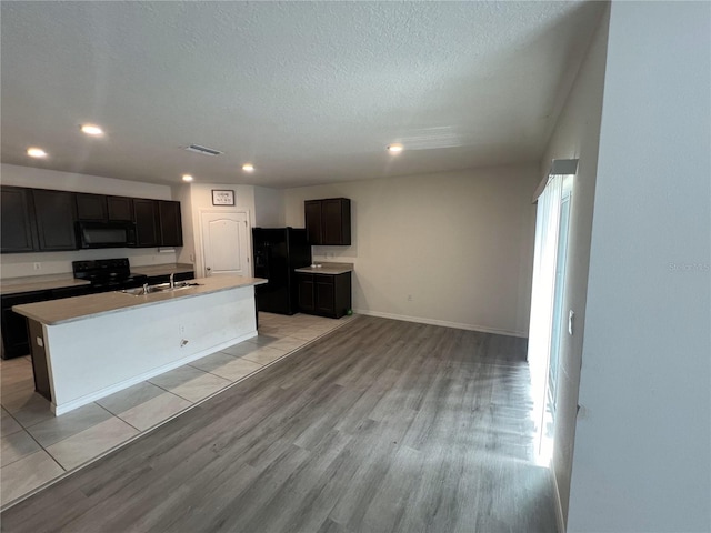 kitchen with light tile patterned flooring, sink, a center island with sink, and black appliances