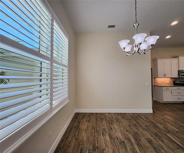 unfurnished dining area featuring dark hardwood / wood-style floors, a healthy amount of sunlight, and an inviting chandelier