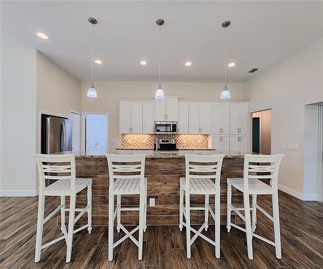 kitchen featuring light stone countertops, appliances with stainless steel finishes, white cabinets, and pendant lighting