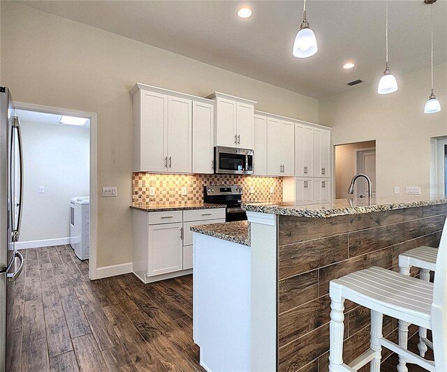 kitchen with white cabinets, stainless steel appliances, hanging light fixtures, and dark stone counters