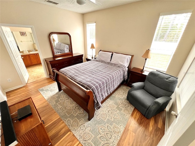 bedroom with light wood-type flooring, connected bathroom, multiple windows, and ceiling fan