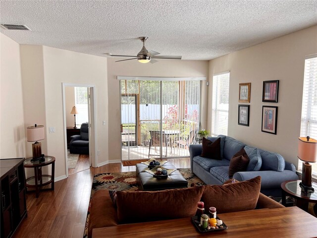 living room featuring a textured ceiling, ceiling fan, a healthy amount of sunlight, and dark wood-type flooring