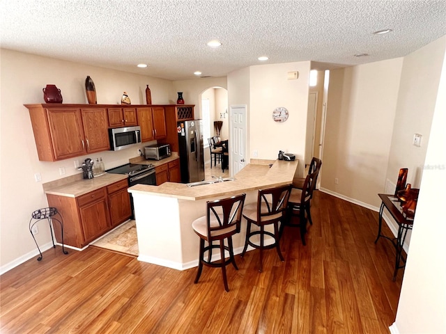 kitchen featuring a textured ceiling, kitchen peninsula, stainless steel appliances, and light hardwood / wood-style flooring