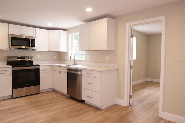 kitchen featuring light wood-type flooring, a sink, white cabinetry, and appliances with stainless steel finishes