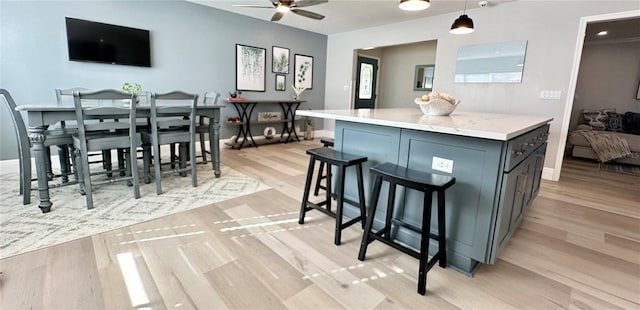 kitchen with ceiling fan, light stone countertops, hanging light fixtures, and light hardwood / wood-style flooring