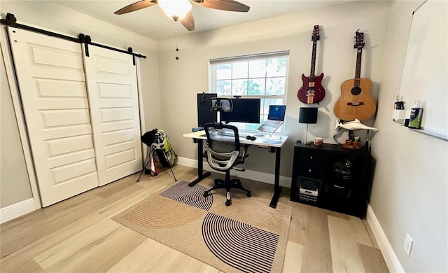 office area with ceiling fan, a barn door, and light wood-type flooring