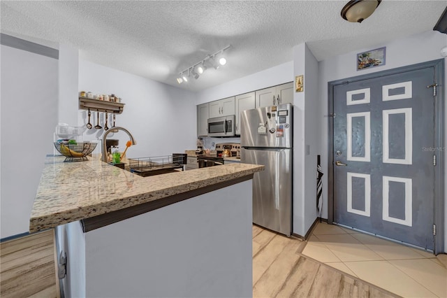 kitchen with stainless steel appliances, kitchen peninsula, track lighting, a textured ceiling, and gray cabinets