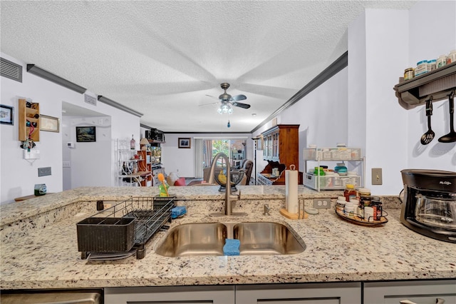 kitchen with a textured ceiling, ceiling fan, ornamental molding, and sink