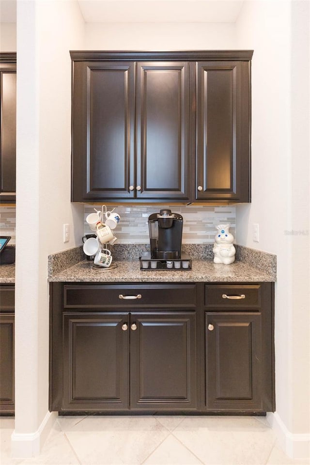 bar with light tile patterned floors, stone counters, decorative backsplash, and dark brown cabinetry