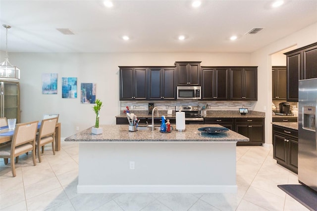 kitchen featuring stainless steel appliances, a center island with sink, light tile patterned floors, and tasteful backsplash