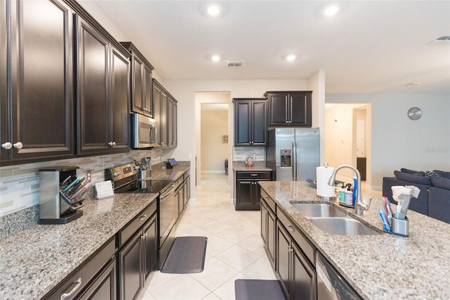 kitchen with stainless steel appliances, sink, light tile patterned floors, backsplash, and light stone countertops