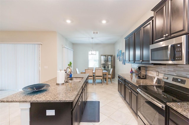 kitchen featuring a kitchen island with sink, appliances with stainless steel finishes, light tile patterned floors, sink, and backsplash