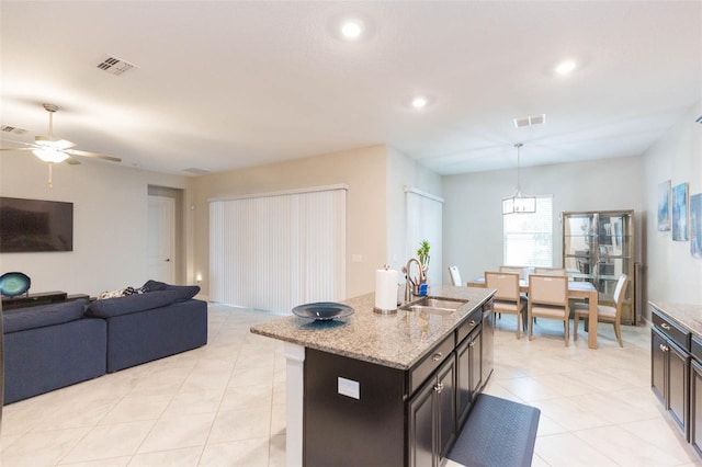 kitchen featuring a center island with sink, ceiling fan, pendant lighting, light stone counters, and sink