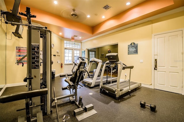 workout area with a raised ceiling and ornamental molding