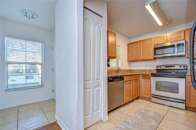 kitchen featuring sink, light stone countertops, light tile patterned floors, a textured ceiling, and appliances with stainless steel finishes