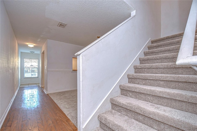 stairway with hardwood / wood-style floors and a textured ceiling