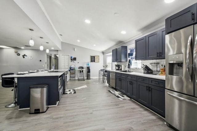 kitchen featuring stainless steel appliances, vaulted ceiling, sink, decorative light fixtures, and an island with sink