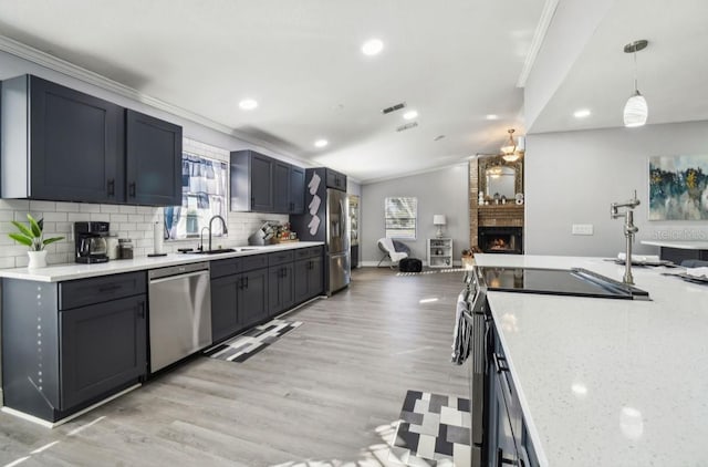 kitchen featuring light stone countertops, a large fireplace, stainless steel appliances, sink, and hanging light fixtures