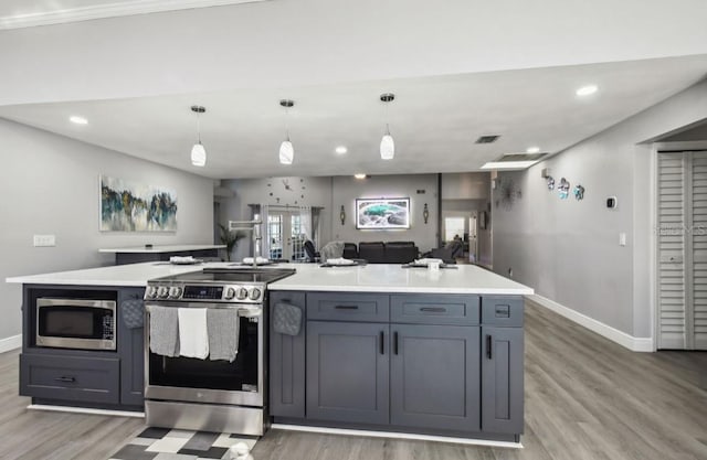 kitchen with gray cabinetry, a center island, decorative light fixtures, appliances with stainless steel finishes, and light wood-type flooring