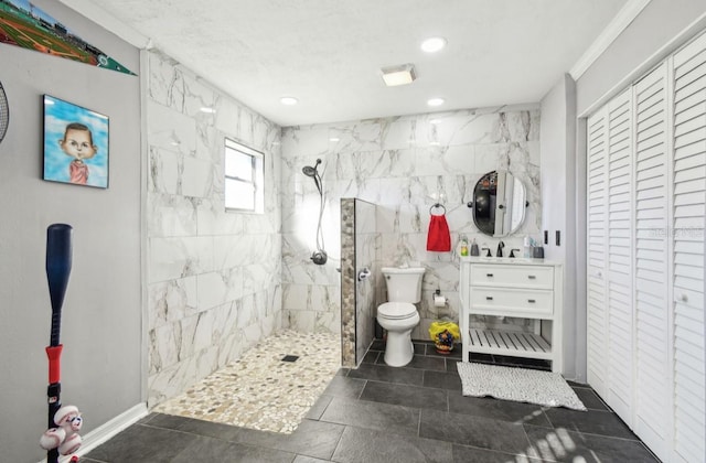 bathroom featuring a tile shower, toilet, vanity, tile walls, and ornamental molding