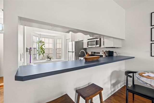 kitchen featuring stainless steel appliances, dark hardwood / wood-style flooring, kitchen peninsula, a breakfast bar area, and white cabinets