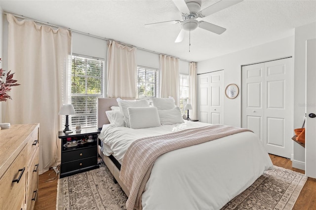 bedroom with a textured ceiling, two closets, ceiling fan, and hardwood / wood-style flooring