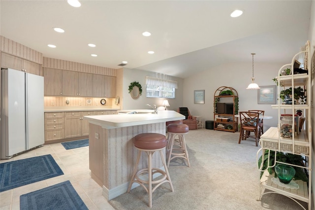 kitchen with sink, decorative light fixtures, light brown cabinets, white fridge, and a kitchen island with sink