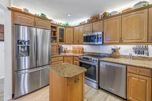 kitchen with light stone countertops, light hardwood / wood-style flooring, a kitchen island, and appliances with stainless steel finishes