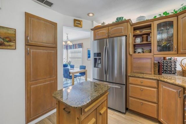 kitchen with light stone countertops, stainless steel fridge with ice dispenser, a kitchen island, and a notable chandelier