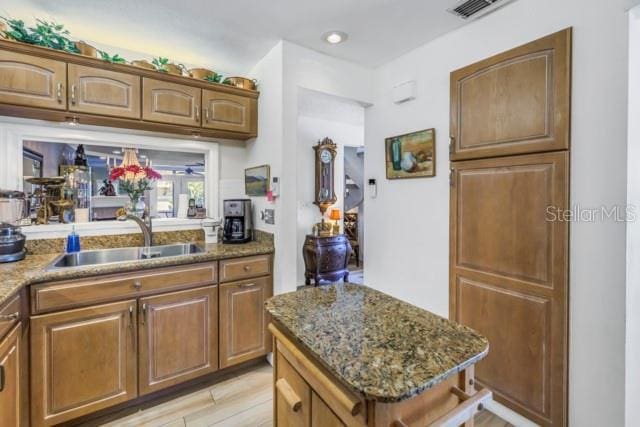 kitchen with stone counters, light wood-type flooring, a center island, and sink