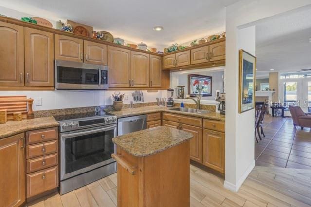 kitchen with appliances with stainless steel finishes, light wood-type flooring, light stone counters, and sink