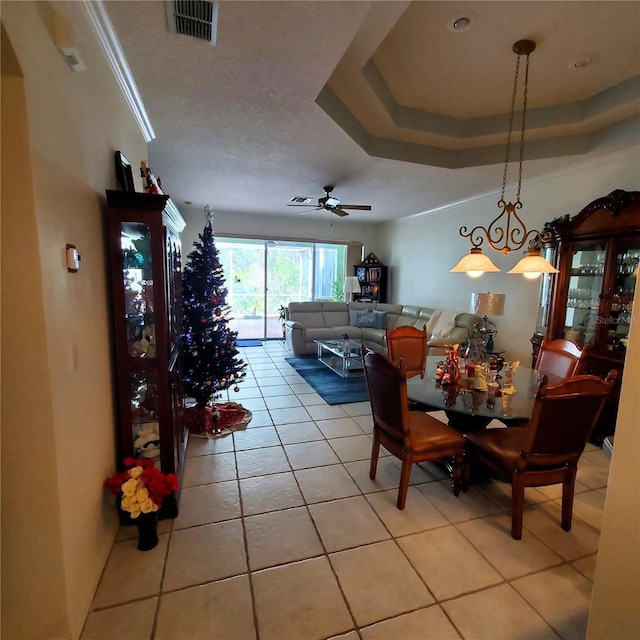 tiled dining room with ceiling fan, a raised ceiling, and ornamental molding