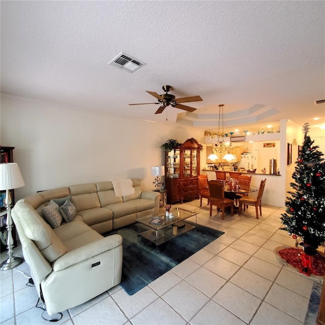 tiled living room with a tray ceiling, a textured ceiling, and ceiling fan with notable chandelier